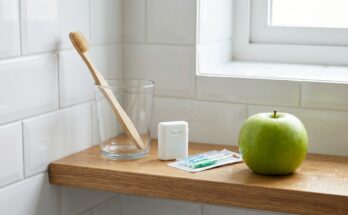 Zahnbürste, Zahnseide und Apfel auf einem Badezimmerregal